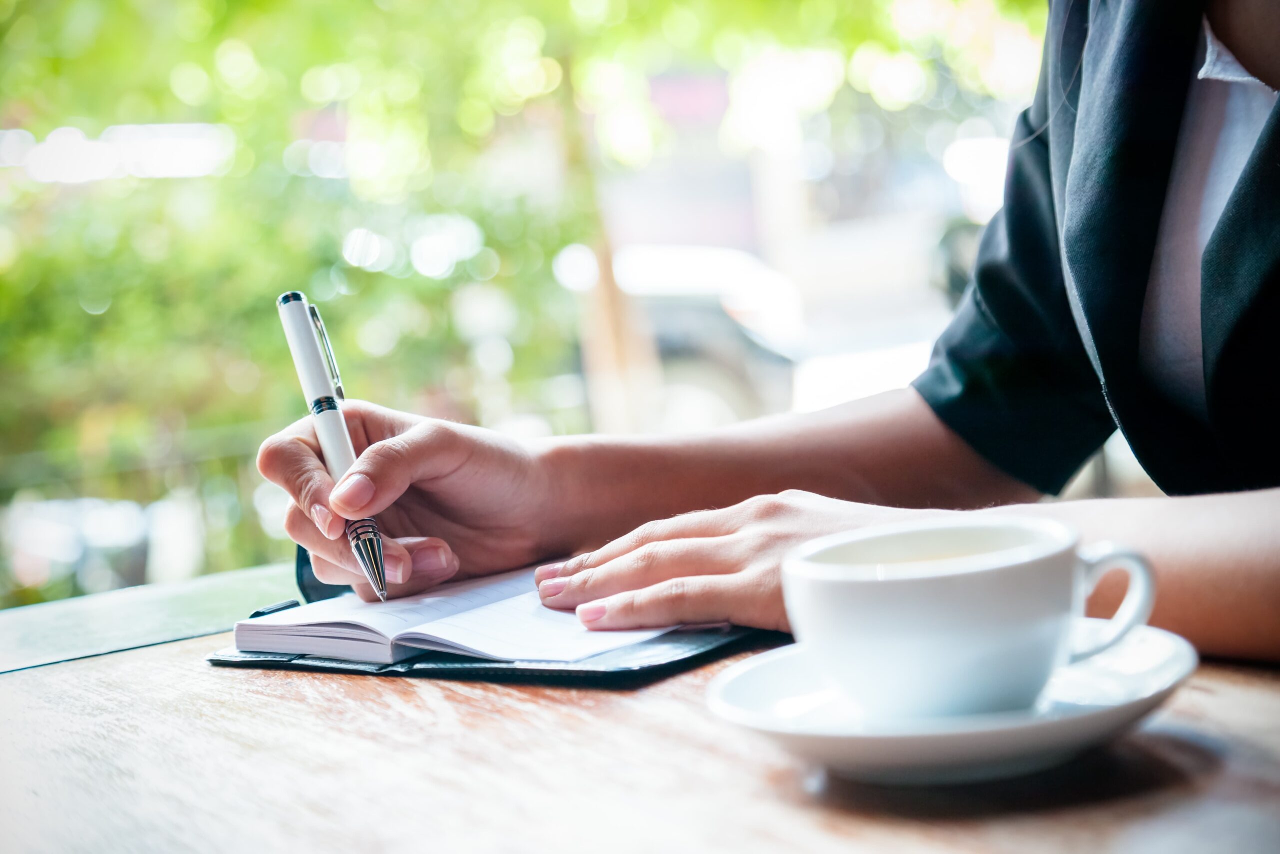 hand writing gratitude entries in a journal beside a warm drink